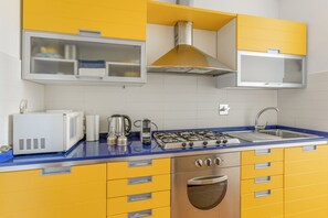 Een keuken met gele kastjes, een blauw aanrecht, een gasfornuis, een magnetron en een spoelbak.