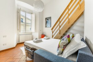 Un dormitorio con cama, ventana, radiador, escalera de madera y una lámpara en el techo.
