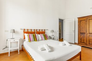 A neatly made bed with pillows, two bedside tables with lamps, a wardrobe, and a door leading to another room. - GuestHost - Charming 80 sqm apartment, for up to 8 people, located on the 4th floor of a building without a lift (40 steep steps at the entrance + 4 floors of stairs, not suitable for people with walking difficulties). The property is located in the hear (Firenze)