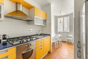 A modern kitchen with yellow cabinets, a gas stove, and a white dining area with a window. - GuestHost - Charming 80 sqm apartment, for up to 8 people, located on the 4th floor of a building without a lift (40 steep steps at the entrance + 4 floors of stairs, not suitable for people with walking difficulties). The property is located in the hear (Firenze)