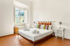 A bedroom with a bed, two bedside tables, a window, and a radiator.