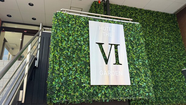 «Hotel VI Garden» -kyltti, jonka taustalla on vihreä, lehtikasveilla peitetty seinä.