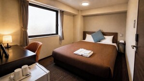 Hotellihuone, jossa on sänky, työpöytä, tuoli, ikkuna verhoilla ja yöpöytä.