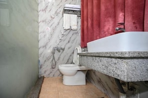 Un baño con pared de mármol, inodoro blanco, encimera de granito y cortina roja.