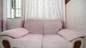 Un canapé beige doté d’un dossier et d’accoudoirs rembourrés, placé devant une fenêtre donnant sur un immeuble.