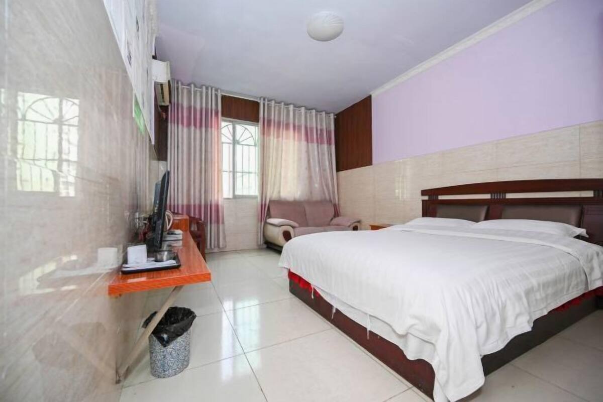 Une chambre d’hôtel équipée d’un lit, d’un bureau, d’une chaise, d’une fenêtre avec des rideaux et d’une poubelle.