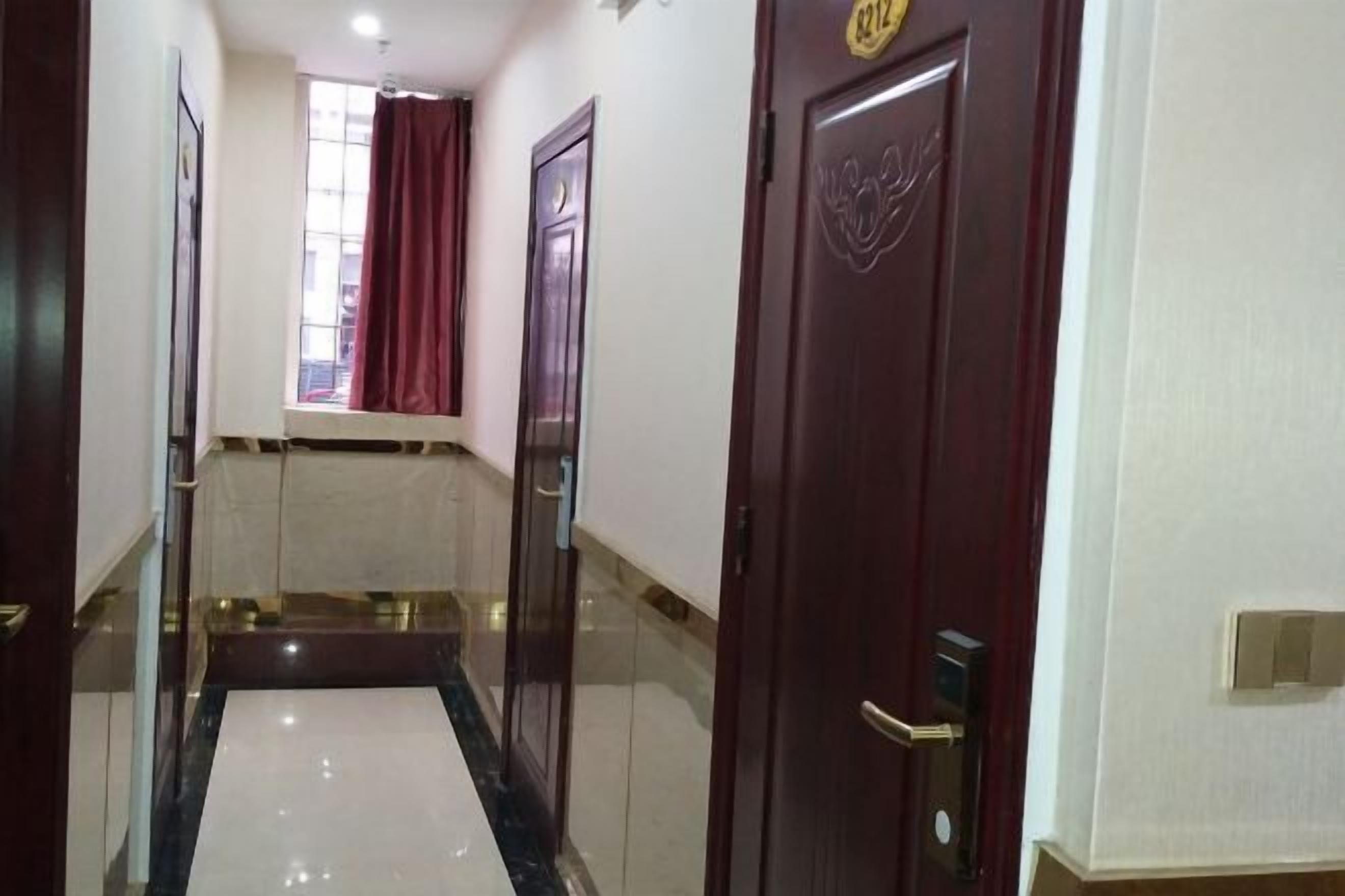 A hotel hallway with a marble floor, a red curtain, and a door with a number plate.