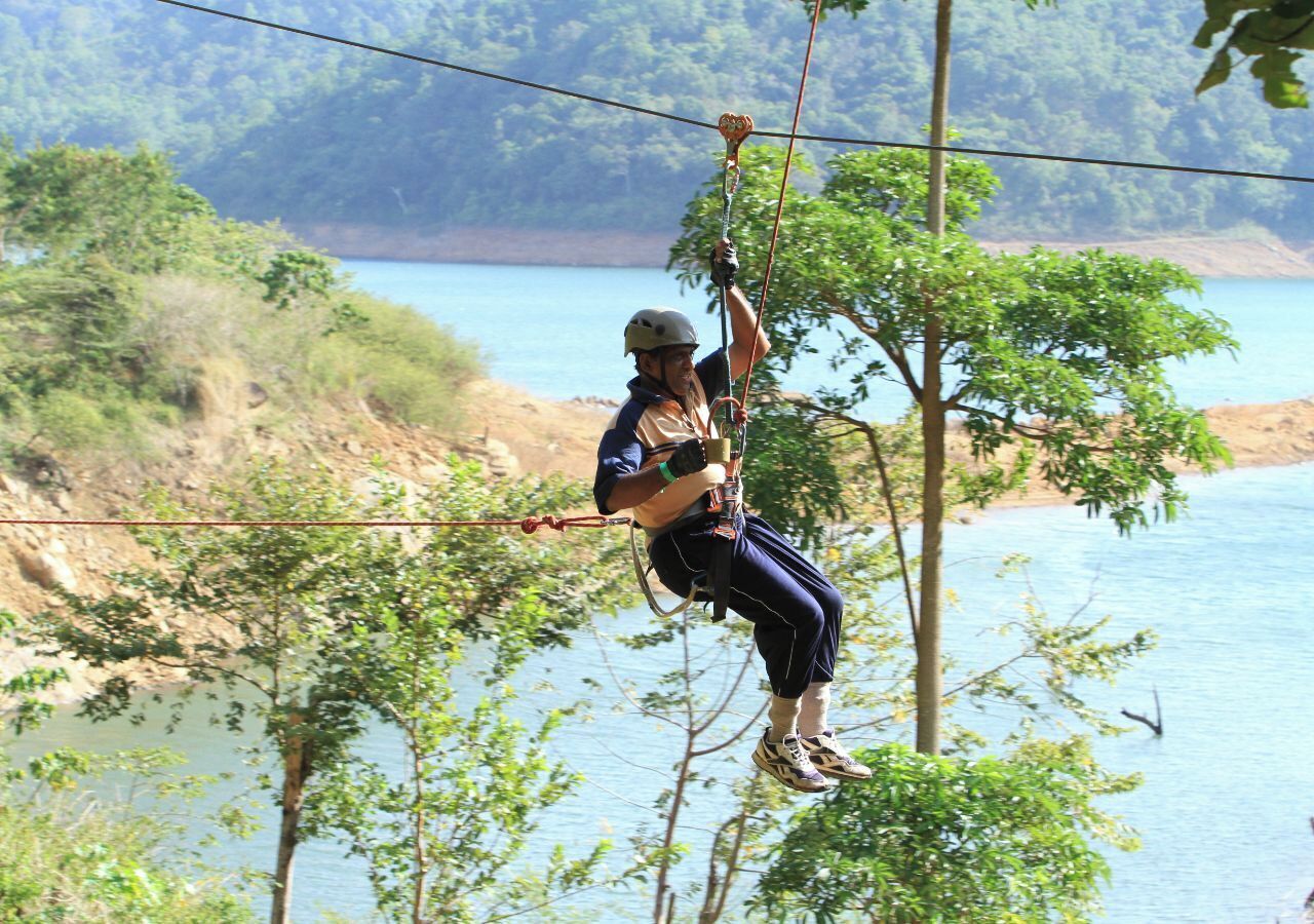 A person zip-lining over a natural landscape with a body of water in the background.