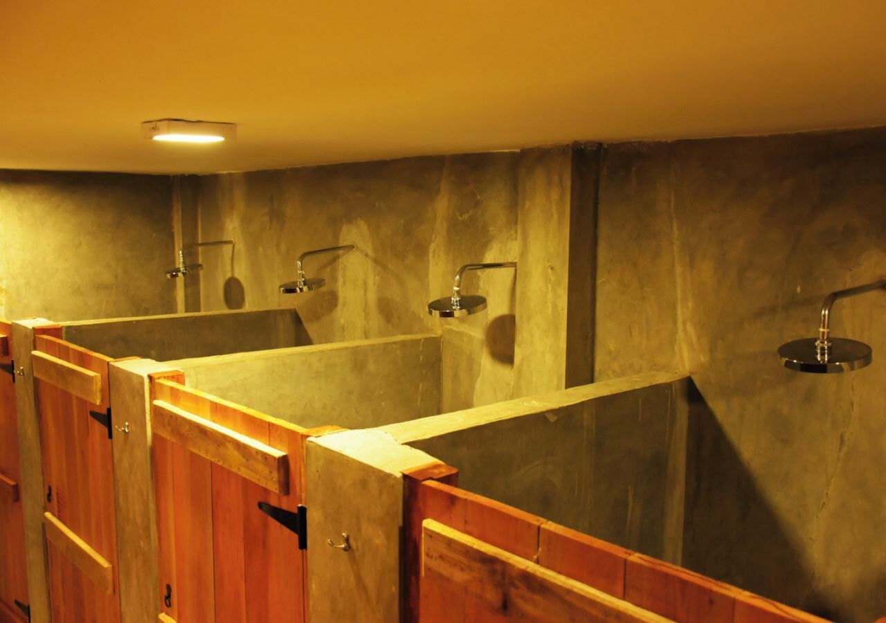 A row of wooden shower stalls with a concrete wall and a ceiling light.