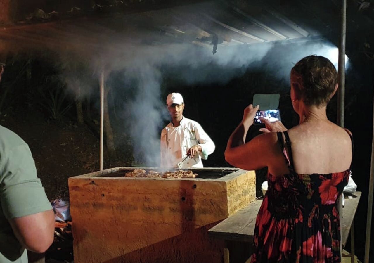 A person cooking outdoors with a large wooden grill, surrounded by smoke.