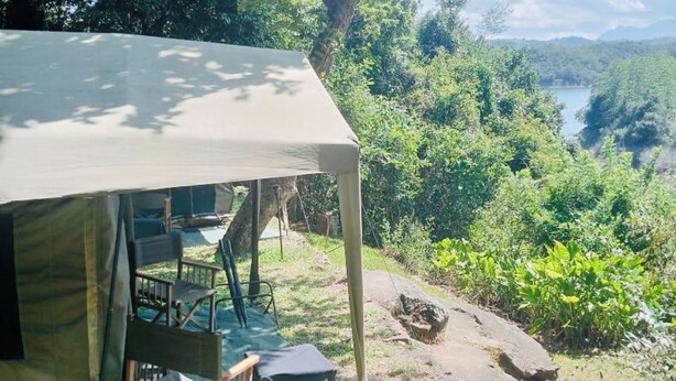A tent with a covered porch, chairs, and a view of a forested area with a river. - Belihuloya Adventure Camp (Rathnapura)