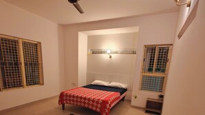 A bedroom with a bed, a ceiling fan, a nightstand, and a window with bars. - Transit Stay (Bengaluru)