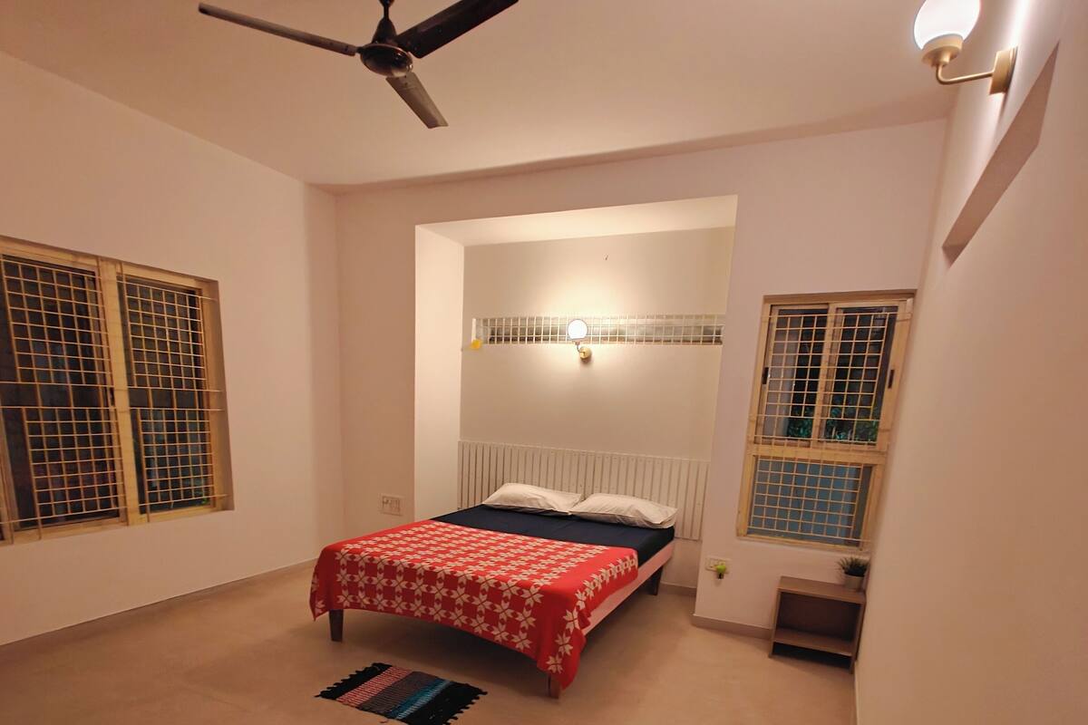 Ein Schlafzimmer mit einem Bett, einem Deckenventilator, einem Nachttisch und einem Fenster mit Gitterstäben.
