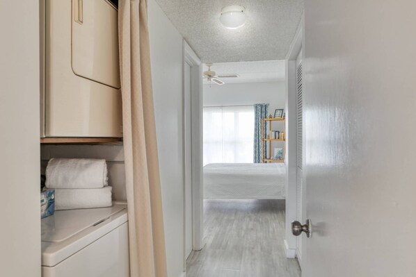 A hallway leading to a bedroom with a bed, a ceiling fan, and a bookshelf.
