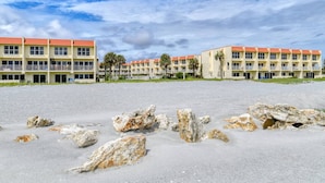A beachfront hotel with multiple-story buildings, a sandy foreground with scattered rocks, and a clear sky. - Ocean and Pool Views! Steps To Beach, Stroll to Restaurants, Shops, and Pier, $300 in Free Tickets! (St. Augustine)