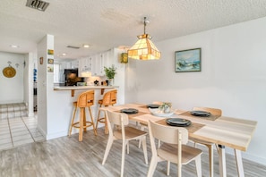 A modern kitchen with white cabinets, a wooden dining table with four chairs, and a hanging pendant light.