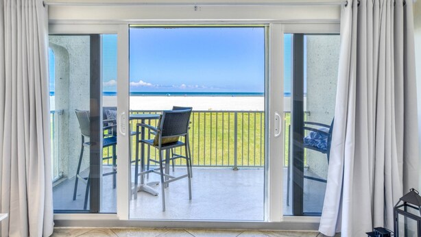 Un balcone con vista sulla spiaggia, una sedia e un tavolo.