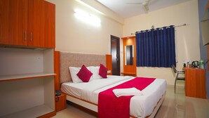 A hotel room with a bed, wooden wardrobe, a mirror, a desk with a kettle, and a ceiling fan. - Hotel Inspira Residency- Near Bombay Hospital (Indore)