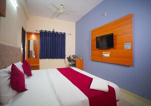 Una habitación de hotel con cama, escritorio, silla, televisor y ventilador de techo.