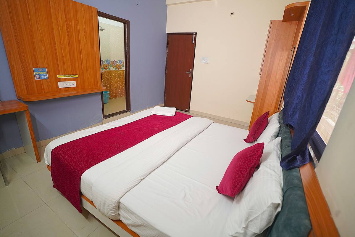 A hotel room with a bed, a wooden wardrobe, a mirror, and a door.