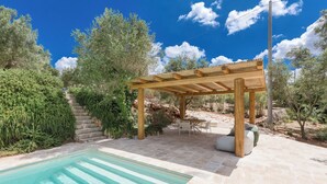 A pool area with a pergola, stone steps, and outdoor furniture.