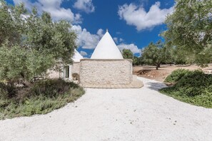 Un sendero de piedra que conduce a una estructura blanca cónica rodeada de olivos.