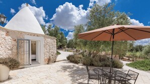 A stone building with a conical roof, a patio with a table and chairs, and an umbrella.