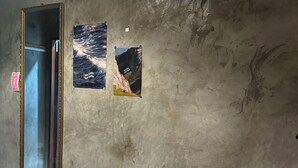 A bathroom with a mirror, two framed pictures on the wall, and a row of slippers on the floor. - Let's Sea Hostel (Krabi)