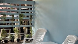 A covered outdoor seating area with white plastic chairs and a table, surrounded by potted plants and a blue wall. - Let's Sea Hostel (Krabi)