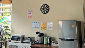 A room with a ceiling fan, a dartboard, a microwave, a coffee maker, a kettle, and a refrigerator. - Let's Sea Hostel (Krabi)