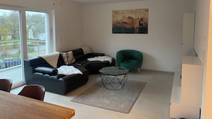 Uma sala de estar moderna com um sofá seccional, uma poltrona verde, uma mesa de centro e uma pintura na parede.