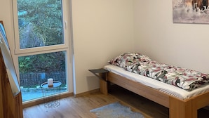 Quarto com cama, janela, um quadro e uma pequena mesa com uma xícara.