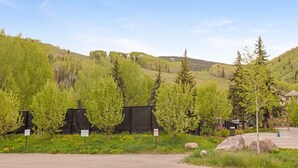 A parking area with a mountain backdrop, trees, and a building with a sign.