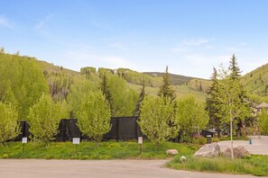 A parking area with a mountain backdrop, trees, and a building with a sign. - Central Vail Condo - Short Walk to Ski & Village (Vail)