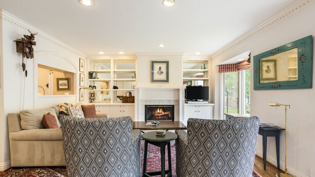 A living room with a fireplace, a sofa, two patterned armchairs, a television, and a bookshelf.