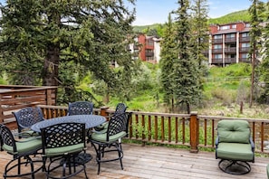 A wooden deck with outdoor furniture, overlooking a mountainous area with trees and a building. - Vail Village Condo - Short Walk to Village Center (Vail)