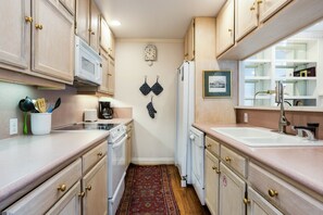 A compact kitchen with wooden cabinets, a microwave, a coffee maker, and a refrigerator.