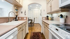 A kitchen with a sink, stove, cabinets, and a dining area with chairs and a table.