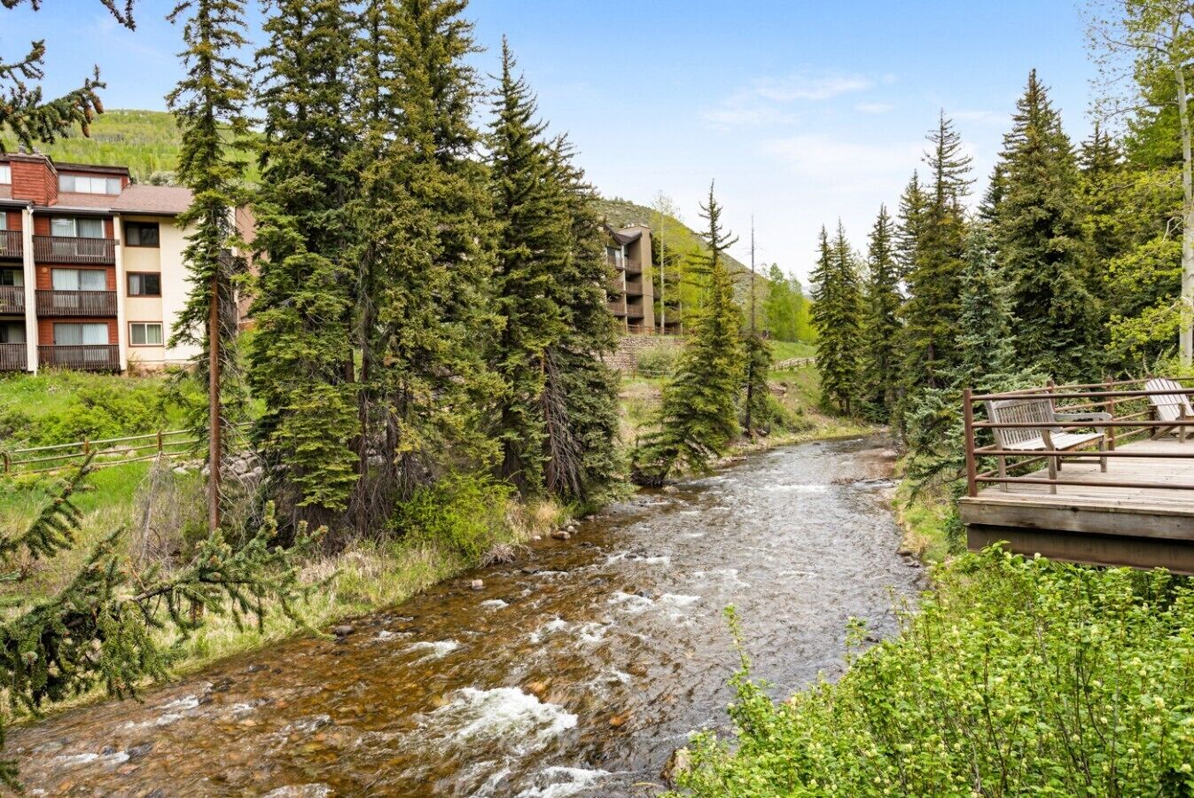 A river flowing through a forested area with a wooden deck and benches.