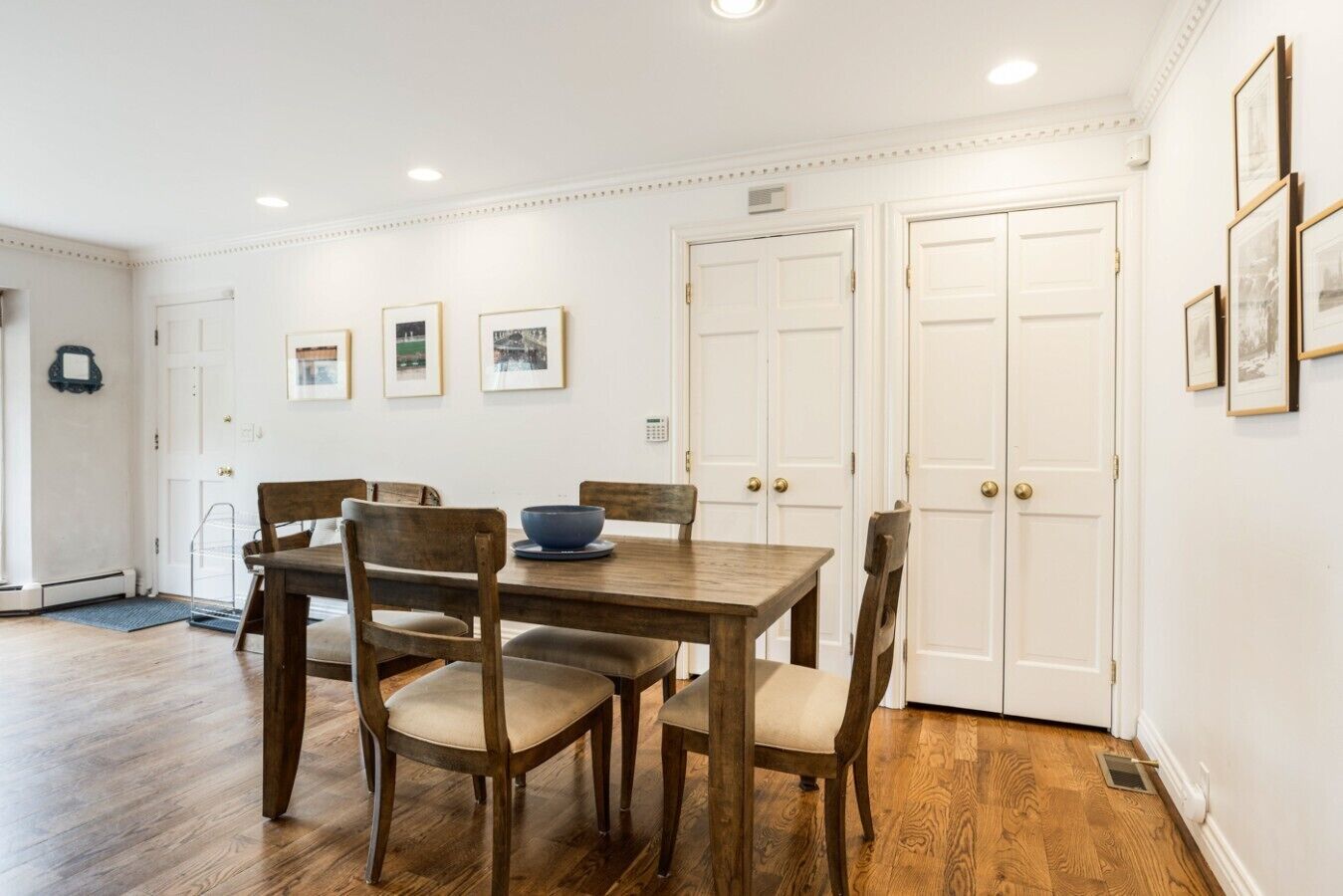 Un comedor con mesa y sillas de madera, cuadros en la pared y puertas blancas.