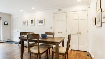 Un comedor con mesa y sillas de madera, cuadros en la pared y puertas blancas.