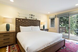 A bedroom with a large bed, wooden headboard, two bedside tables with lamps, a window with a view of greenery, and a balcony with outdoor furniture. - Central Vail Condo - Short Walk to Ski & Village (Vail)