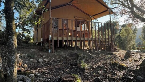 A wooden cabin with a covered deck, surrounded by trees and natural terrain.