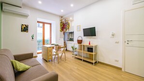 A modern living room with a sofa, a dining table with chairs, a TV mounted on the wall, and a door. - Lo Spagnoletto (Naples)