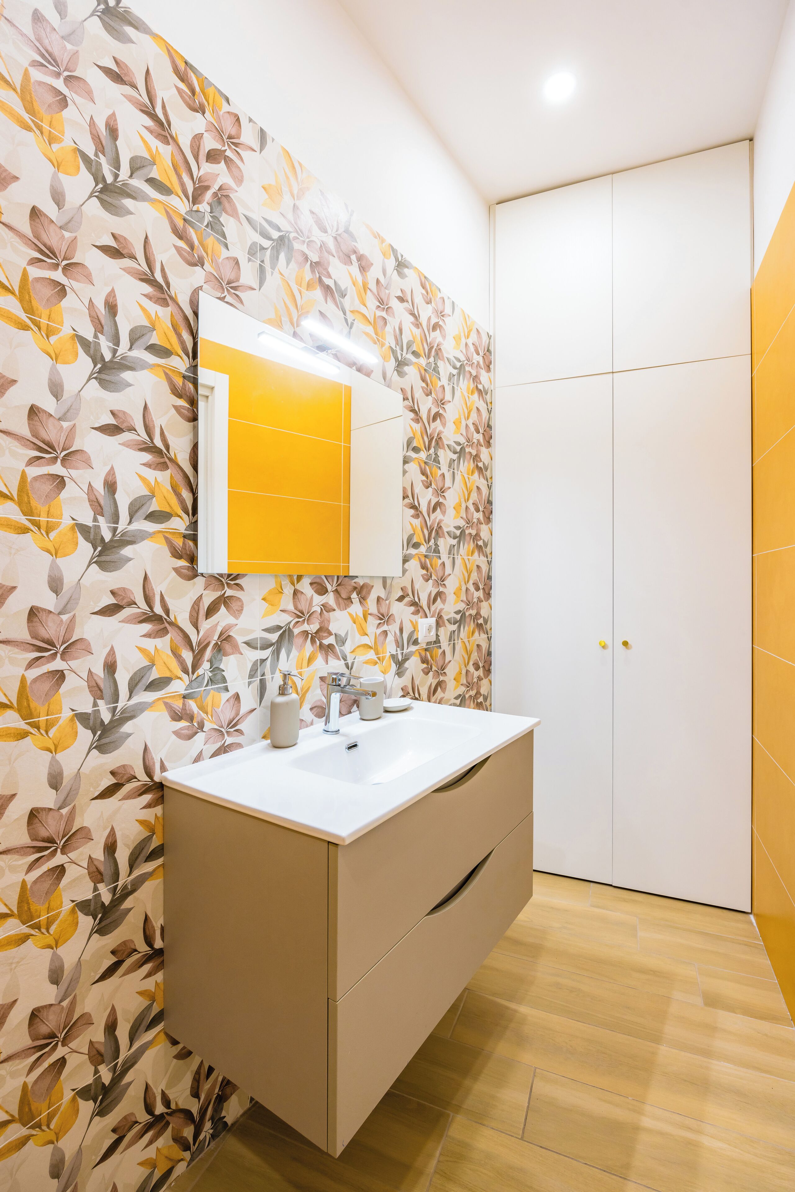Un baño con tocador blanco, espejo y papel tapiz floral.
