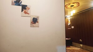 Un couloir doté d’un plancher en bois et d’un mur orné de trois tableaux encadrés. Une porte se trouve sur la droite et un luminaire est fixé au plafond.