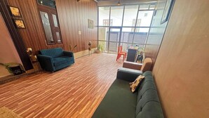 Une pièce spacieuse avec un plancher en bois, un canapé vert, un canapé bleu et une petite table avec des chaises.