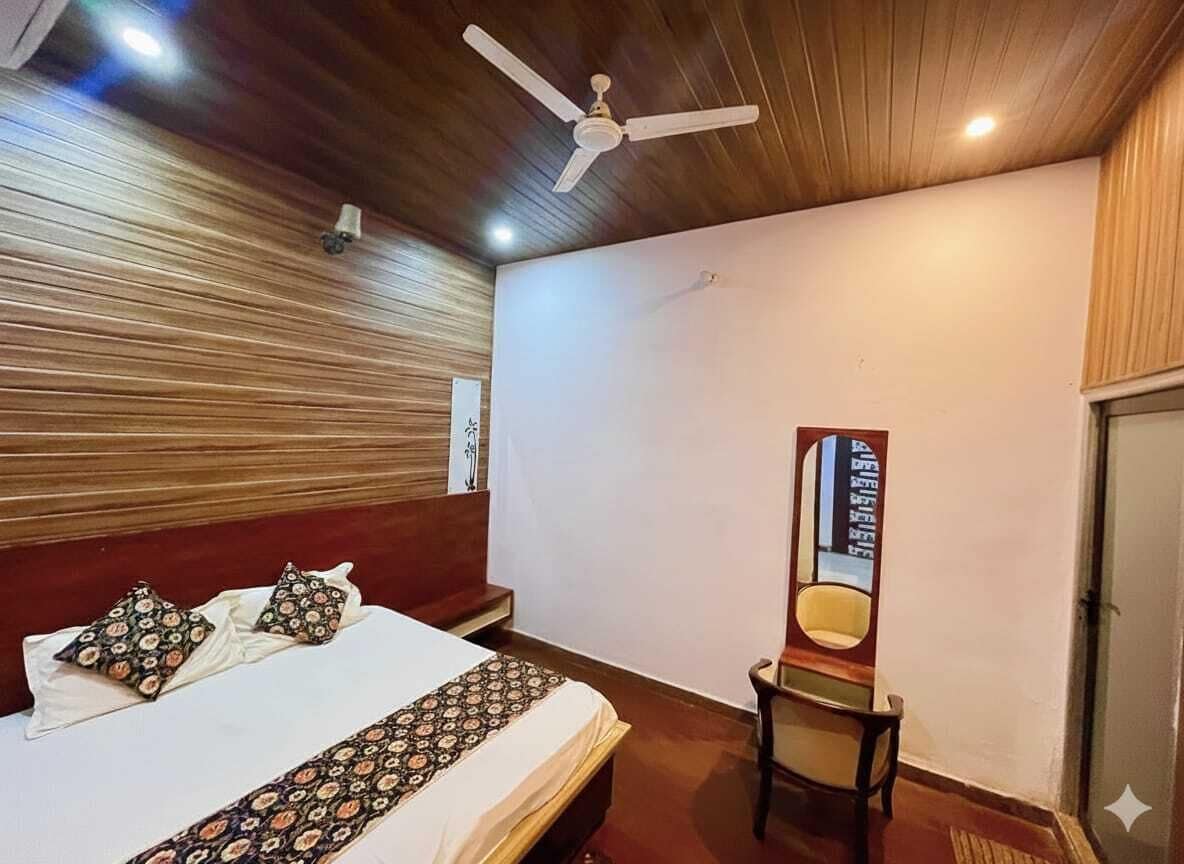 Una habitación de hotel con cama, una silla, un ventilador de techo y un espejo fijado a la pared.