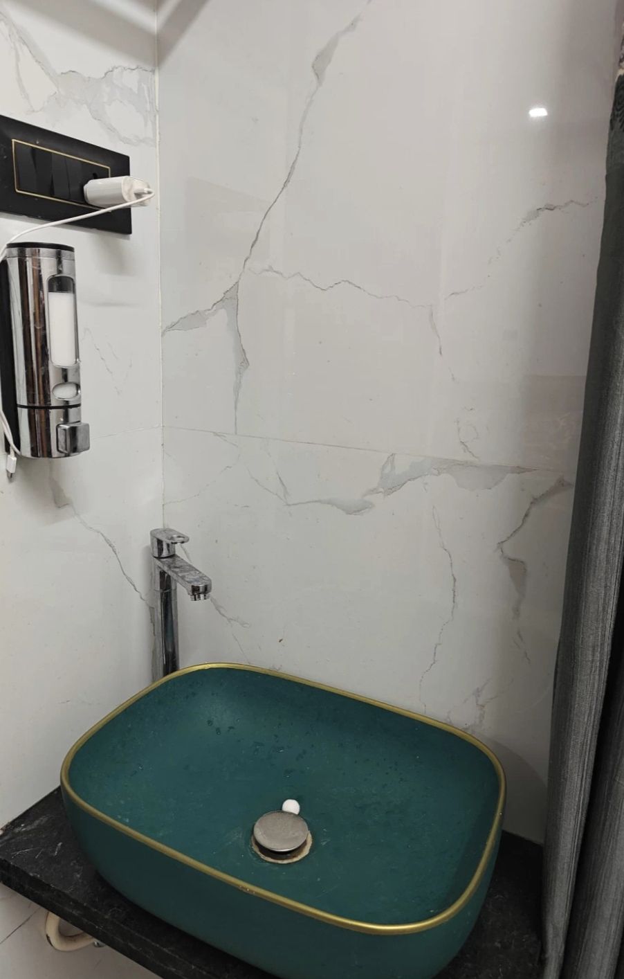 Une salle de bain avec un mur en marbre, un lavabo vert et un espace douche.