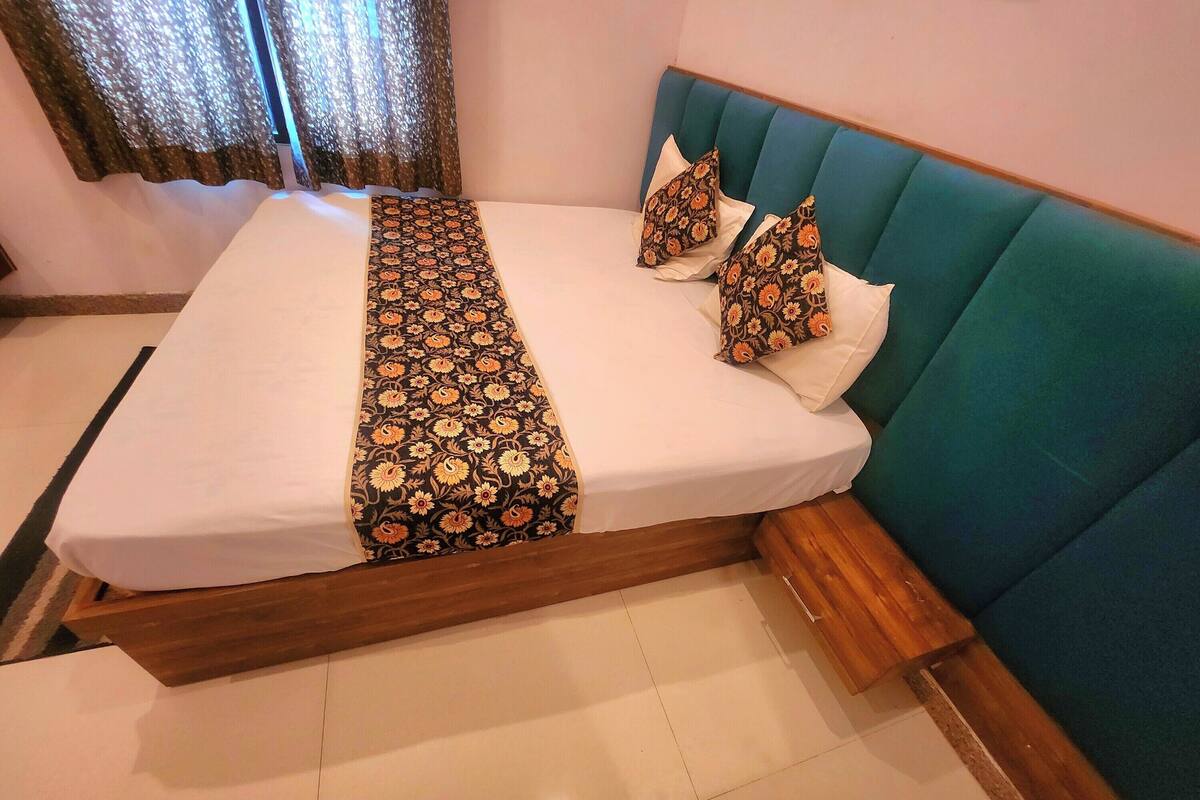 Una cama bien hecha con ropa de cama estampada con motivos florales, un cabecero tapizado en color verde azulado y almohadas a juego.